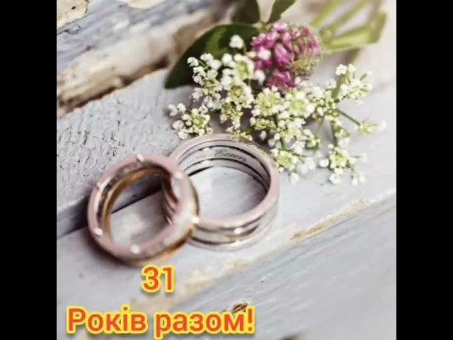 Два обручальні кільця та квіти на дерев'яній дошці.