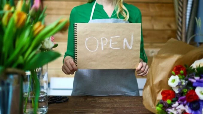 Людина тримає табличку OPEN серед квітів для відкриття закладу.